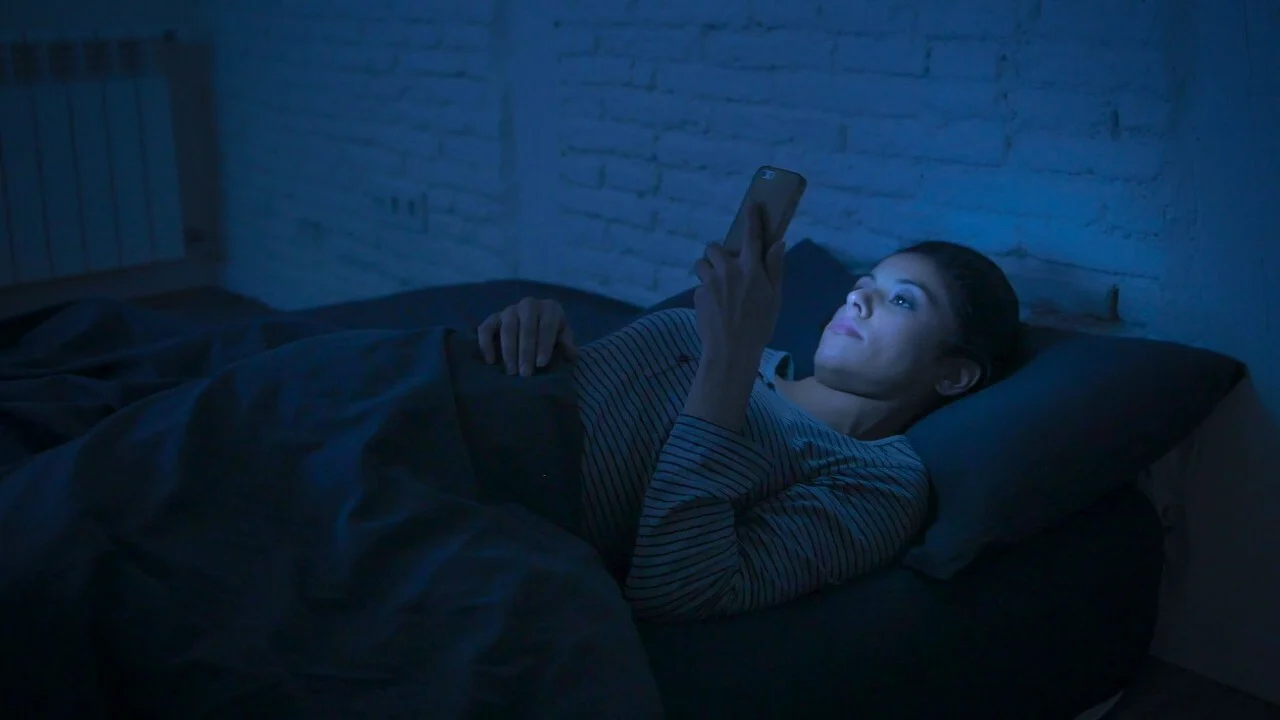 Teenager looking at a bright phone screen in a dark bedroom showing blue light exposure