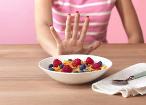 A woman pushing a bowl of cereal with fruit away